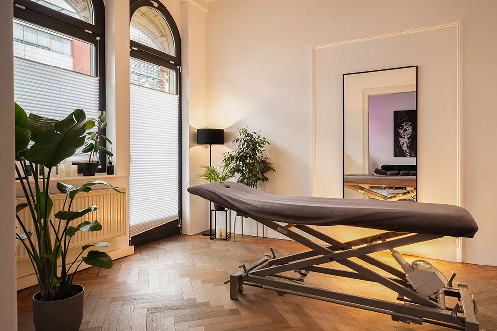 Heller Behandlungsraum mit Therapieliege und Bogenfenstern